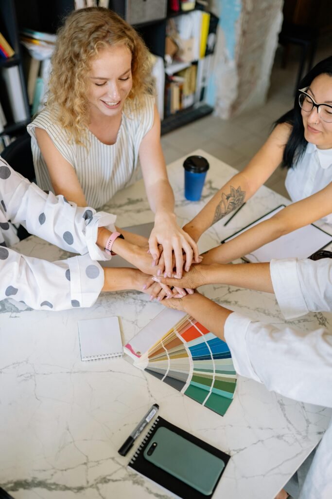 Diverse colleagues uniting hands together over color palette at the workplace, symbolizing teamwork.